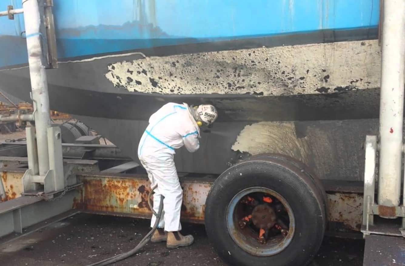 person in PPE performing sandless blasting on the side of a large boat - Dustless Sandblasting Near Me