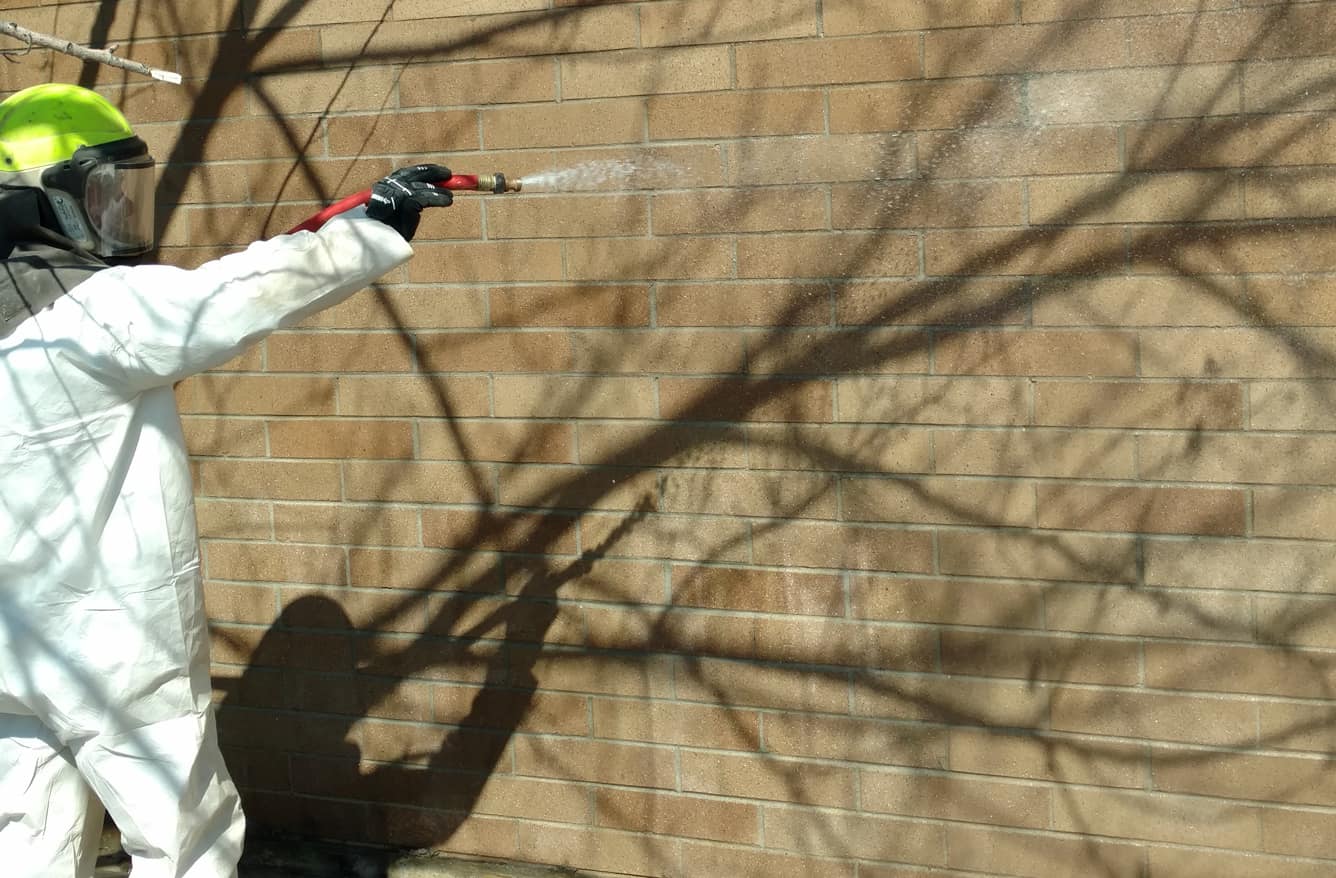 person in safety suit spraying brick wall to remove graffiti